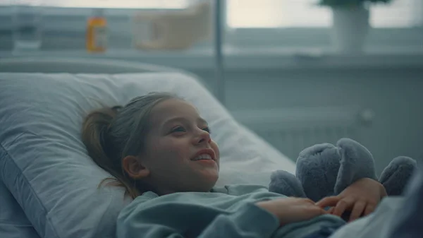 Portrait fille couché lit d'hôpital étreignant jouet. Médecin visitant le patient en salle. — Photo
