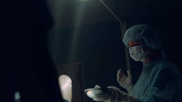 Nurse handing instruments surgeon holding sterile tools in dark emergency room. — Stock Photo, Image