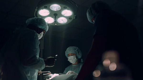 Zespół chirurgów operujący na ciemnym, sterylnym oddziale. Pracownicy medyczni ratujący pacjenta. — Zdjęcie stockowe