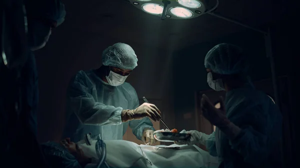 Equipe médica realizando operação cirúrgica na sala de emergência do hospital escuro. — Fotografia de Stock