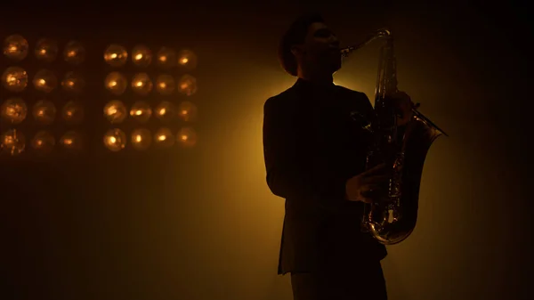 Homem de silhueta saxofonista tocando instrumento no palco. Cara jogando sax no clube. — Fotografia de Stock