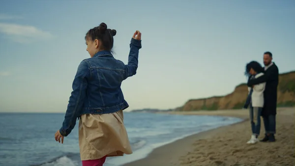 Little girl playing beach on family trip. Parents spending time together on sea.