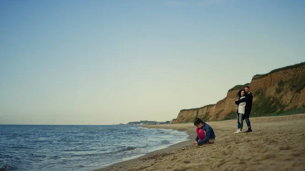 Rodzina odpoczywa na plaży przy spokojnych falach rozbijających. Ludzie cieszą się wakacjami nad oceanem. — Zdjęcie stockowe