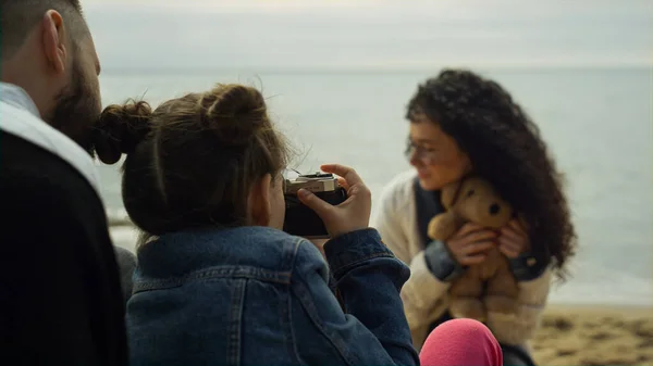 Familia jugando cámara fotográfica en la playa del mar. Padres niño fotografiando oso de peluche — Foto de Stock