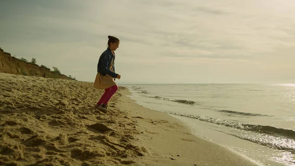 Gün batımında sahilde oynayan küçük bir kız. Mutlu çocuk deniz kenarında tek başına dinleniyor.