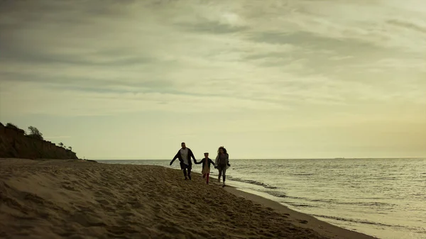 Familia caminando por la playa mañana. Jóvenes corriendo al amanecer vacío en la orilla del mar. — Foto de Stock