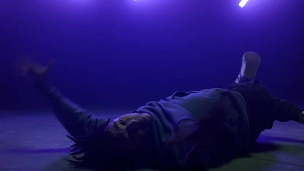 Élégant breakdancer corps mobile couché piste de danse dans les lumières ultraviolettes club. — Photo