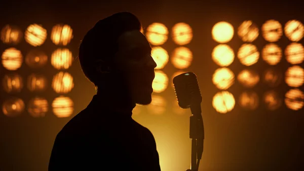 Silhouette singing man vocalist using microphone on show stage nightclub closeup