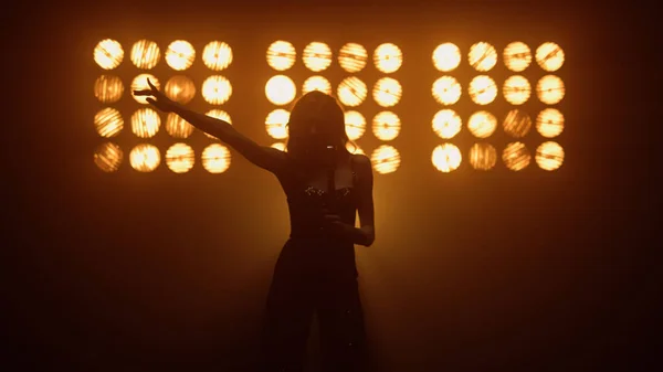 Stüdyo ışıklarında şarkı söyleyen siluet kız müzisyen. Sahnede gösteri yapan kadın — Stok fotoğraf