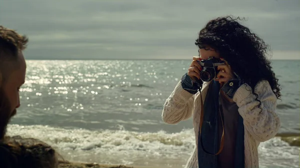 在海浪海滩上给家人拍照的女人。卷发女孩用相机. — 图库照片