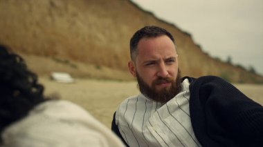 Sakin bir çift deniz plajı pikniğinde birlikte dinleniyor. Erkek kız arkadaşının saçına dokunuyor..