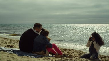Anne babası sahilde poz veriyor. Genç bir aile, parlak okyanusun kenarında fotoğraf çekiyor.