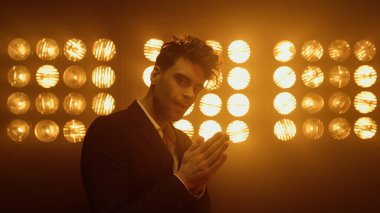 Model adam gece kulübünde avuçlarını ovalıyor. Esmer adam sahneye çıkıyor.