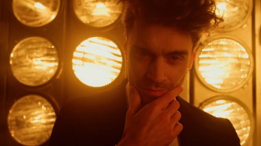 Gece kulübü ışıklarında dönen erkek model kapanıyor. Adam kendinden emin duruyor.