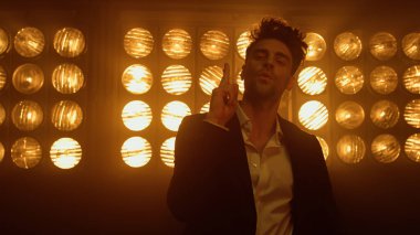 Gece kulübünde parmak şıklatma pozu veren seksi adam. Erkek model sahnede duruyor..