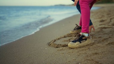 Çocuk deniz doğasında kumsalda ayakta duruyor. Küçük kız bacakları, spor ayakkabıları dışarıda oynuyor..