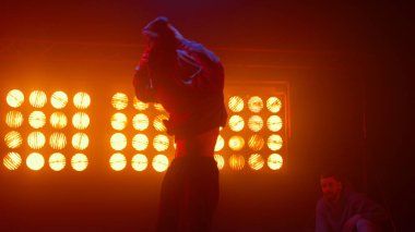 Güçlü adam yel değirmenini icra ediyor. Dansçı numaralar gösteriyor.