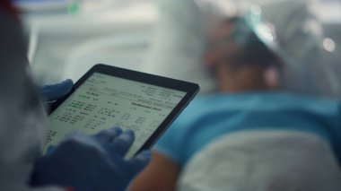Doktor tablet ekranı tutuyor. Koğuştaki hastanın tıbbi geçmişini kontrol ediyor..