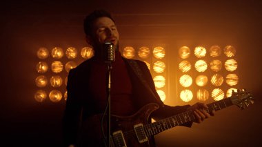 Sahne ışıkları altında şarkı söyleyen dansçı mikrofonu kapat. Gitar tutan müzisyen.