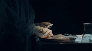 Hemşire elleri karanlık ameliyathanede dikiş atmak için gerekli aletleri hazırlıyor..