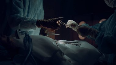 Cerrahlar tıbbi kıyafetin içinde dikiş kesiği atıyor. Karanlık ameliyathane kapalı..