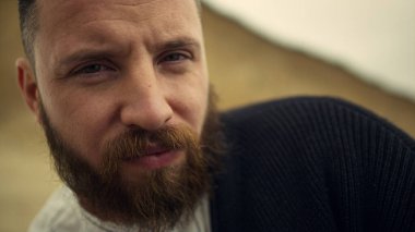 Sakallı adam kameraya bakıyor. Sahilde dinlenen ciddi bir adam yüzü..