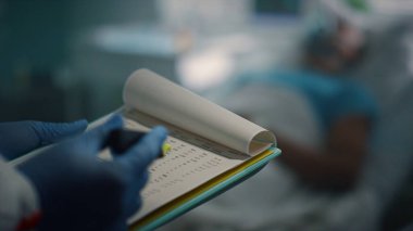 Yatağında oksijen maskesi olan hasta bir hasta. Doktor tıbbi geçmişini kontrol ediyor. Yakın plan.