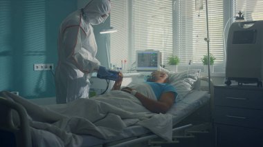 Enfeksiyon ünitesi koğuşunda kan basıncını sphygmomanometre ile ölçen bir doktor.