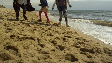 Aile bacakları deniz kıyısında birlikte plaj oynar. Okyanus dalgaları arasında yürüyen eğlenceli insanlar..