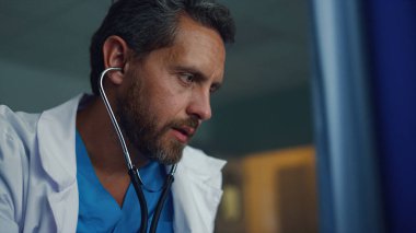 Sakallı terapist klinikteki kimliği belirsiz hastanın kalp atışlarını dinliyor.