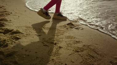 Çocuk yürüyen deniz plajı. Küçük kız bacakları kaçıyor, dalgalar sahile vuruyor.