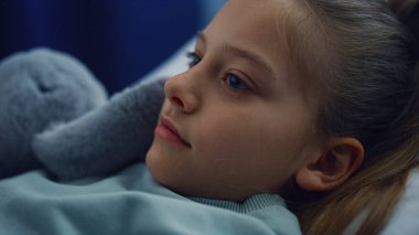 Pediyatri bölümünde hastane kontrolünde pelüş oyuncakla yatakta yatan portre kızı..