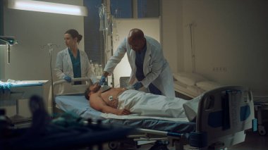 Doktor hastane koğuşunda defibrilatör kullanıyor. Klinik personeli hastanın hayatını kurtarıyor.