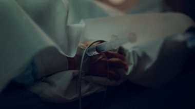 Hasta eli şırınga kateteri yakın çekim. Bilinmeyen adam hastane yatağında yatıyor.. 
