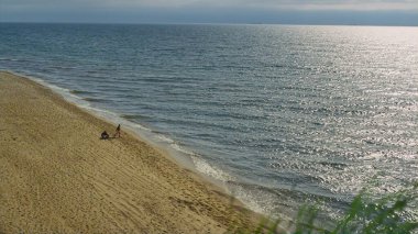Deniz manzarasında çim rüzgâr plajı esiyor. Gökyüzü manzaralı insanlar kumsalda oturuyor..