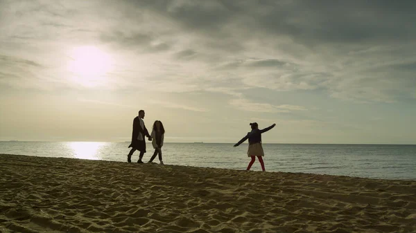 Χαρούμενη οικογένεια πηγαίνει παραλία ηλιοβασίλεμα ουρανό ωκεανό. Άνθρωποι ομάδα με τα πόδια στη θάλασσα ακτή. — Φωτογραφία Αρχείου