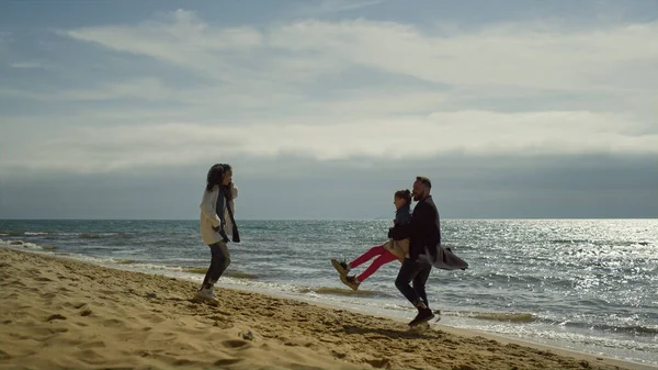 Anne ve babası deniz kenarında kumsalda oynuyorlar. Neşeli insanlar doğada eğleniyor..