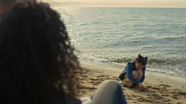 Aile sahilde yan yana oturuyor. Deniz kıyısında kumdan kale inşa eden neşeli çocuk..