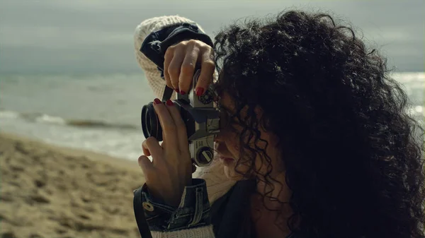 Ισπανίδα φωτογραφίζει την παραλία δίπλα στην ήρεμη θάλασσα. Σγουρά μαλλιά γυναίκα λήψη φωτογραφιών. — Φωτογραφία Αρχείου