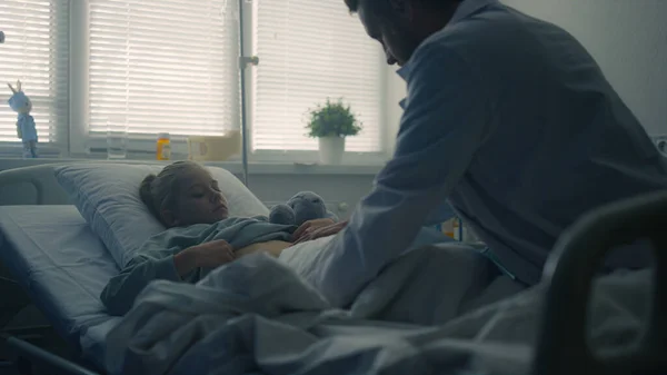 病気の女の子の医師のベッドの後ろのビューの近くに座っている。病院での健康診断. — ストック写真