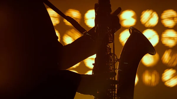 Saxofonista silhueta mãos tocando instrumento musical em holofotes de perto. — Fotografia de Stock