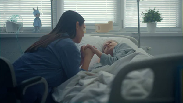 Ragazzina sdraiata letto d'ospedale. Donna di sostegno in visita tenendo mano bambino. — Foto Stock