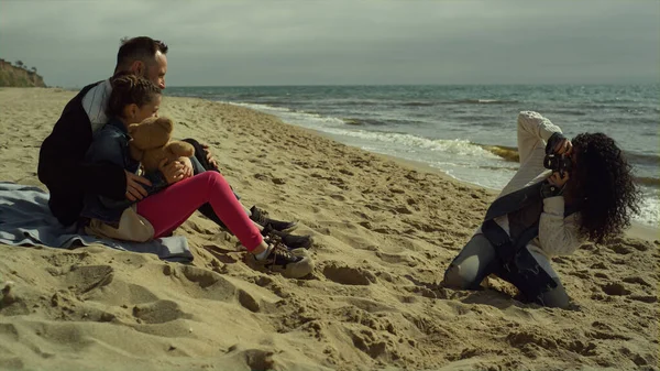 Okyanus kumsalında fotoğraf çeken neşeli bir aile. İnsanlar kumda birlikte rahatlar.. 