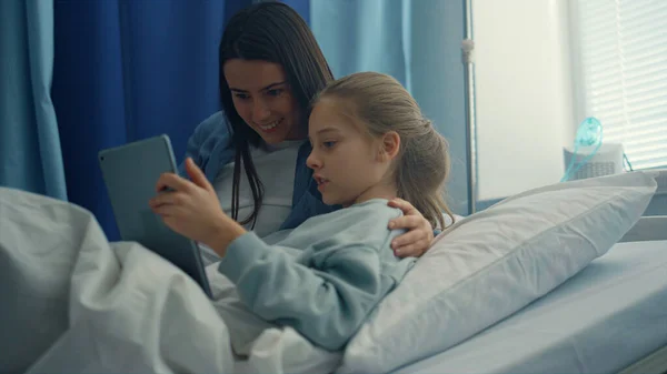 Sorridente mamma visita figlia giocare su tablet computer insieme in camera d'ospedale — Foto Stock