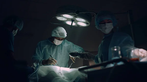 Zespół lekarzy wykonujący operacje chirurgiczne na sali operacyjnej ciemnego szpitala. — Zdjęcie stockowe