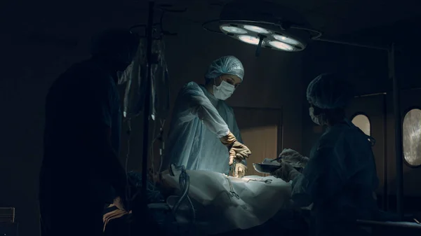 Selbstbewusster Chirurg operiert in dunkler steriler Klinik-Notaufnahme. — Stockfoto