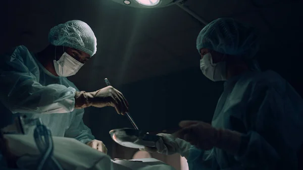 Chirurg operujący w ciemnym oddziale ratunkowym. Pracownik medyczny biorący krwawe tampony. — Zdjęcie stockowe