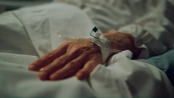 Hand with IV catheter in ward bed closeup. Aged patient undergo clinic treatment — ストック写真