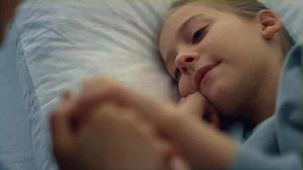 Мила дівчина лежить в лікарняному ліжку портрет. Мати обережно тримає дитячу руку крупним планом . — стокове фото