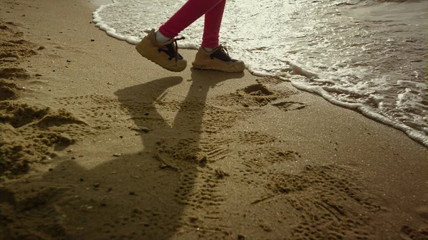 Çocuk yürüyen deniz plajı. Küçük kız bacakları kaçıyor, dalgalar sahile vuruyor.